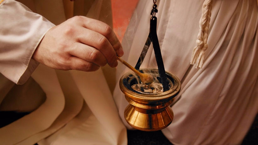 a hand placing incense into a golden thurible