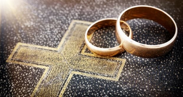 2 gold wedding bands on a black bible with a gold embossed cross