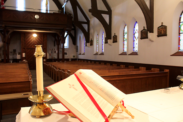 An open Lectionary with a candle behind it, all sitting on an altar facing an empty church