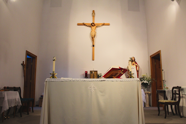 The sanctuary space at St. Cornelius mission, with an altar in the middle, and a large crucifix hanging on the wall