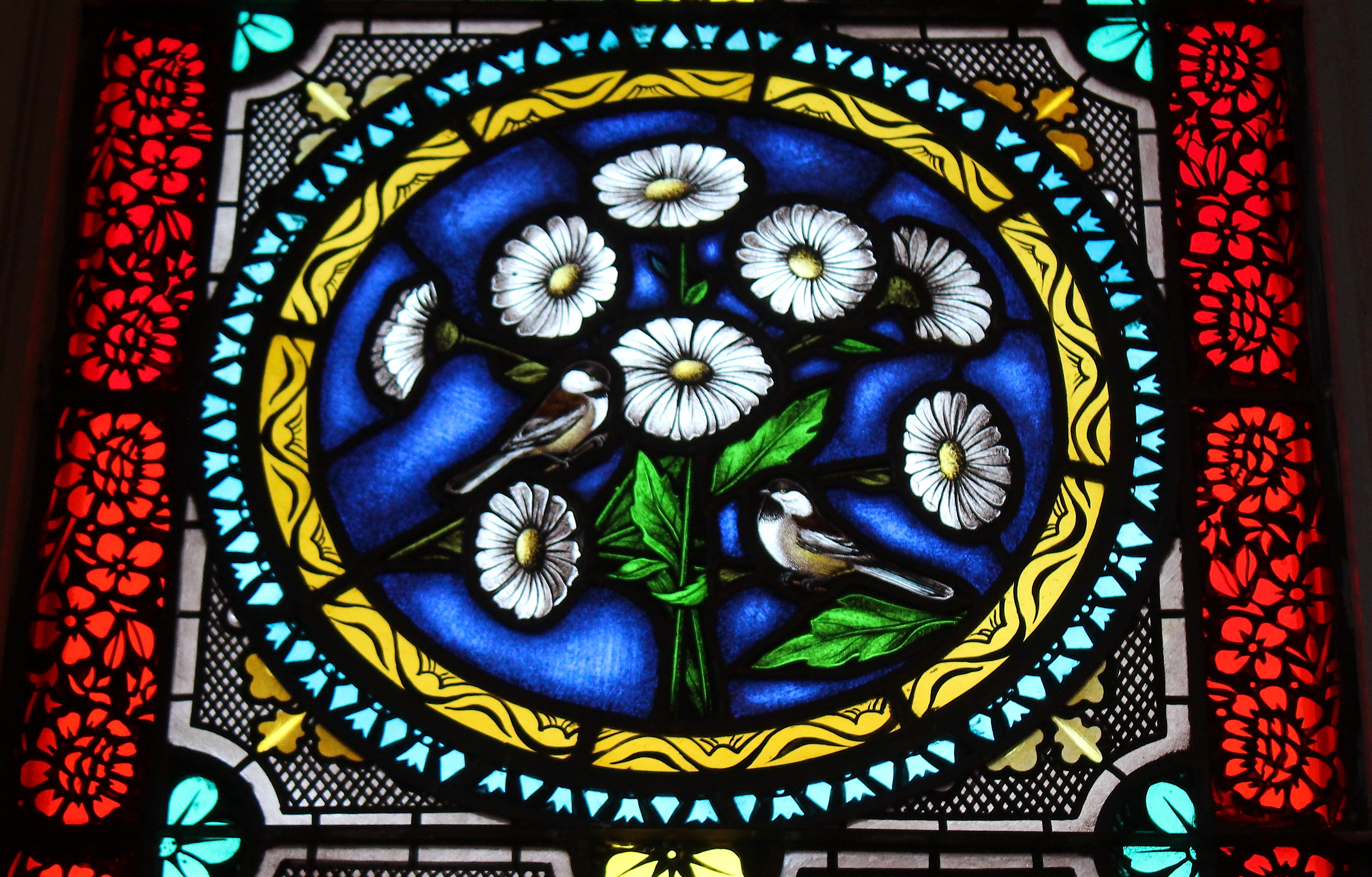 A stained glass window of white daisies and 2 small sparrows